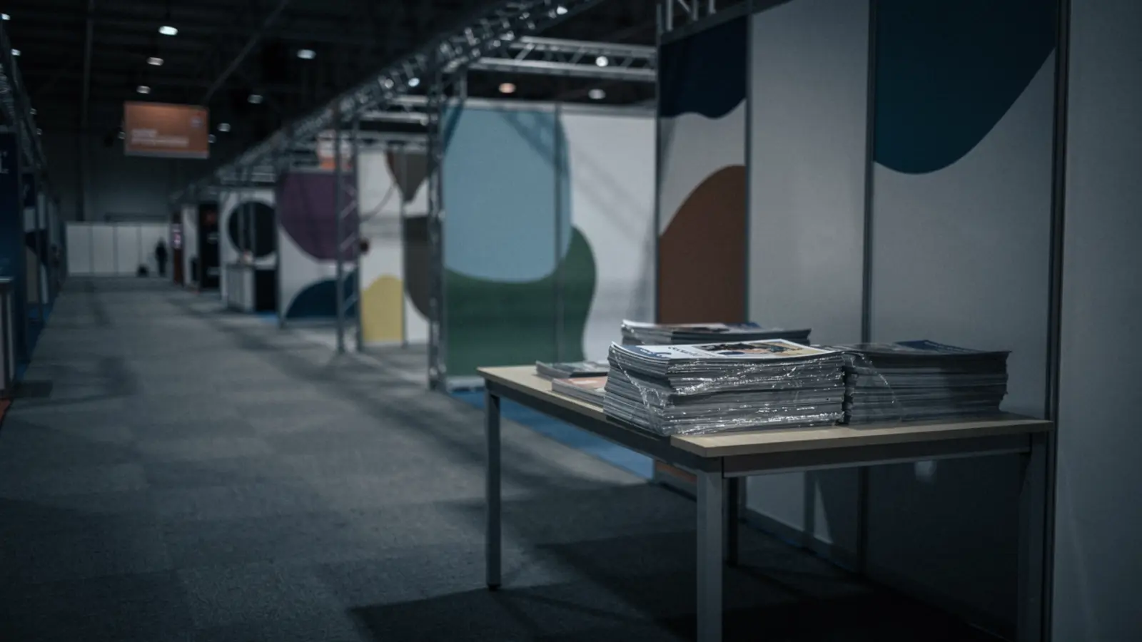 A closed trade show booth after hours, shrink-wrapped brochures in an empty convention hall