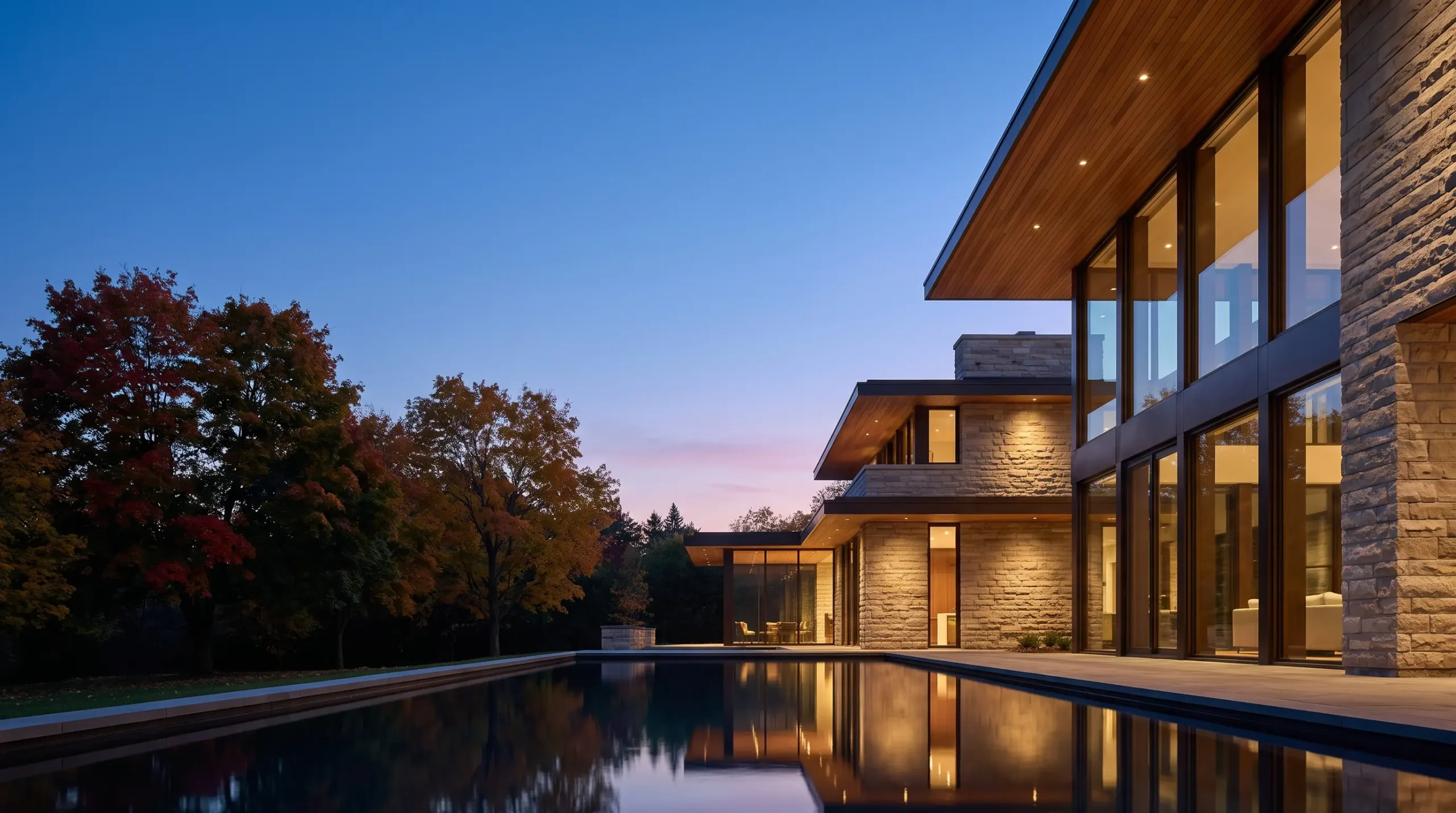 A contemporary custom home at blue hour, glowing from inside, with a reflecting pool in the foreground